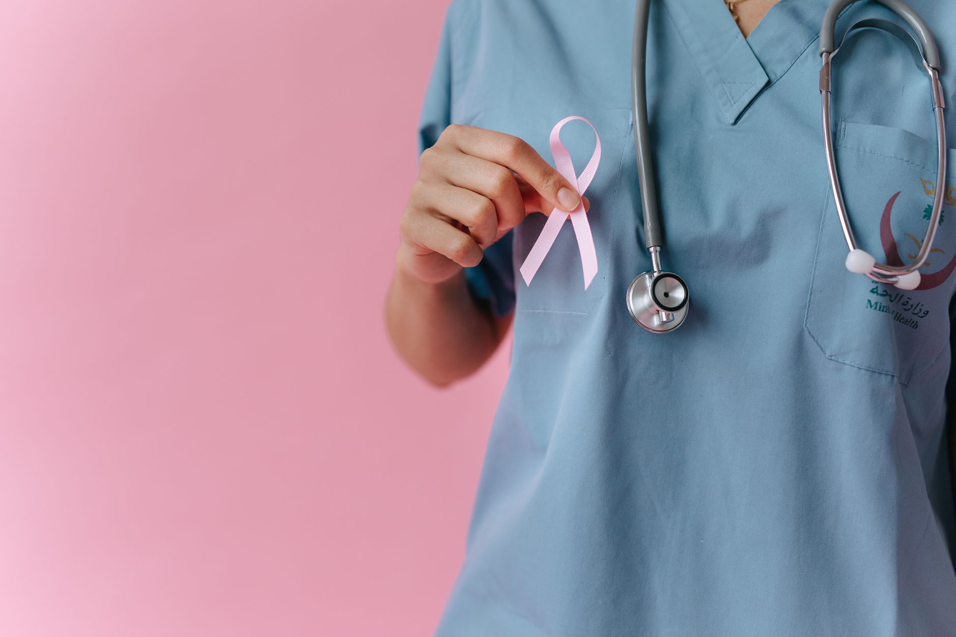 Healthcare worker in scrubs holds a pink breast cancer awareness ribbon symbolizing support. — 4 Primary Aspects Of Physiothe