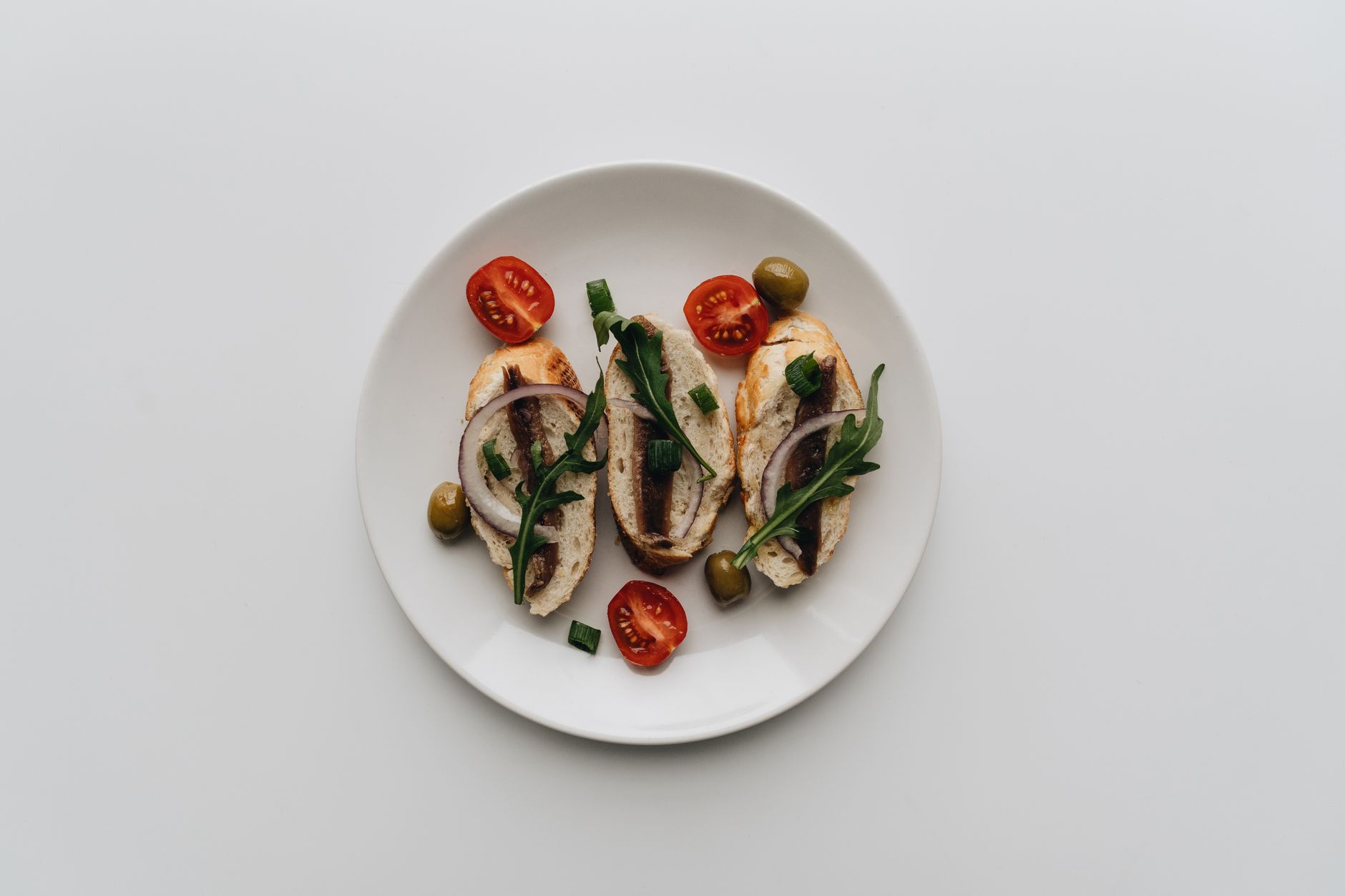 A top view of delicious bruschetta with anchovies, olives, and cherry tomatoes on a white plate. — 5 Perfect Nutritious Foods