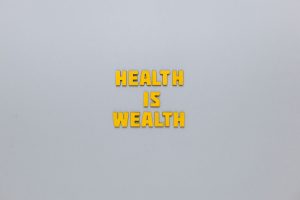 Inspirational phrase 'Health is Wealth' in bold yellow letters on a neutral gray background. — Awareness of meeting your high