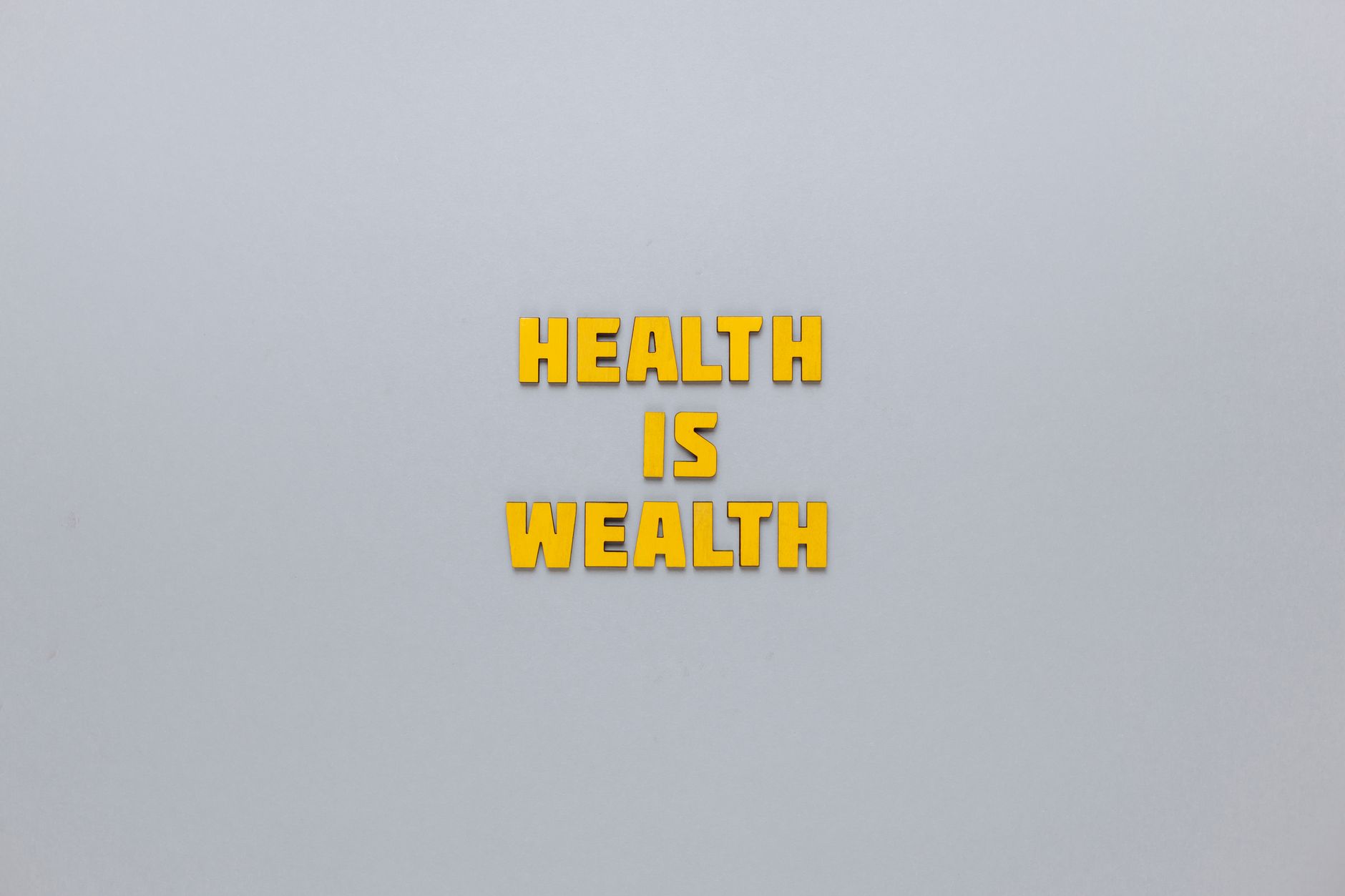 Inspirational phrase 'Health is Wealth' in bold yellow letters on a neutral gray background. — Awareness of meeting your high