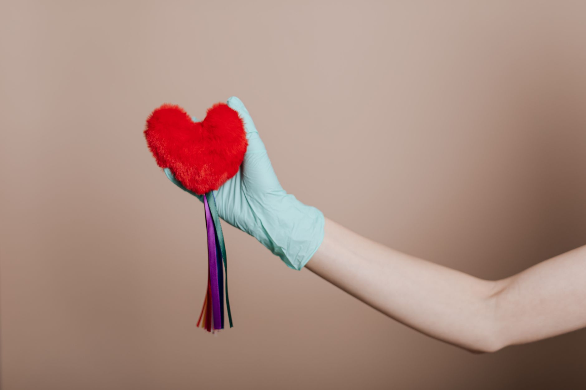 A latex-gloved hand holds a red heart-shaped plush with colorful strings, symbolizing love and safety. — CBD for Skincare