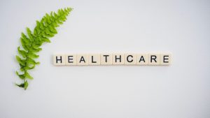 Healthcare word spelled with Scrabble tiles next to a green fern leaf on a white background. — Comprehensive Addiction Treatm