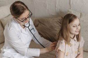 A doctor with a stethoscope examining a smiling girl during a medical check-up at home. — dry hair should pay special