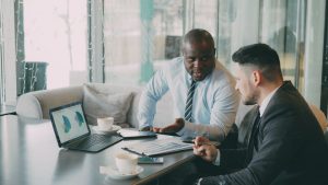 Two businessmen discussing data at a cafe while enjoying coffee. — Evaluating Forex Brokers: Key Factors to Consider