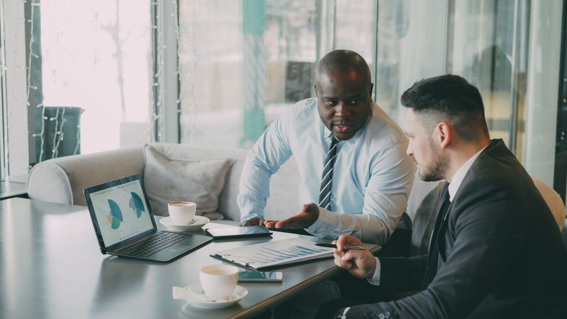 Two businessmen discussing data at a cafe while enjoying coffee. — Evaluating Forex Brokers: Key Factors to Consider