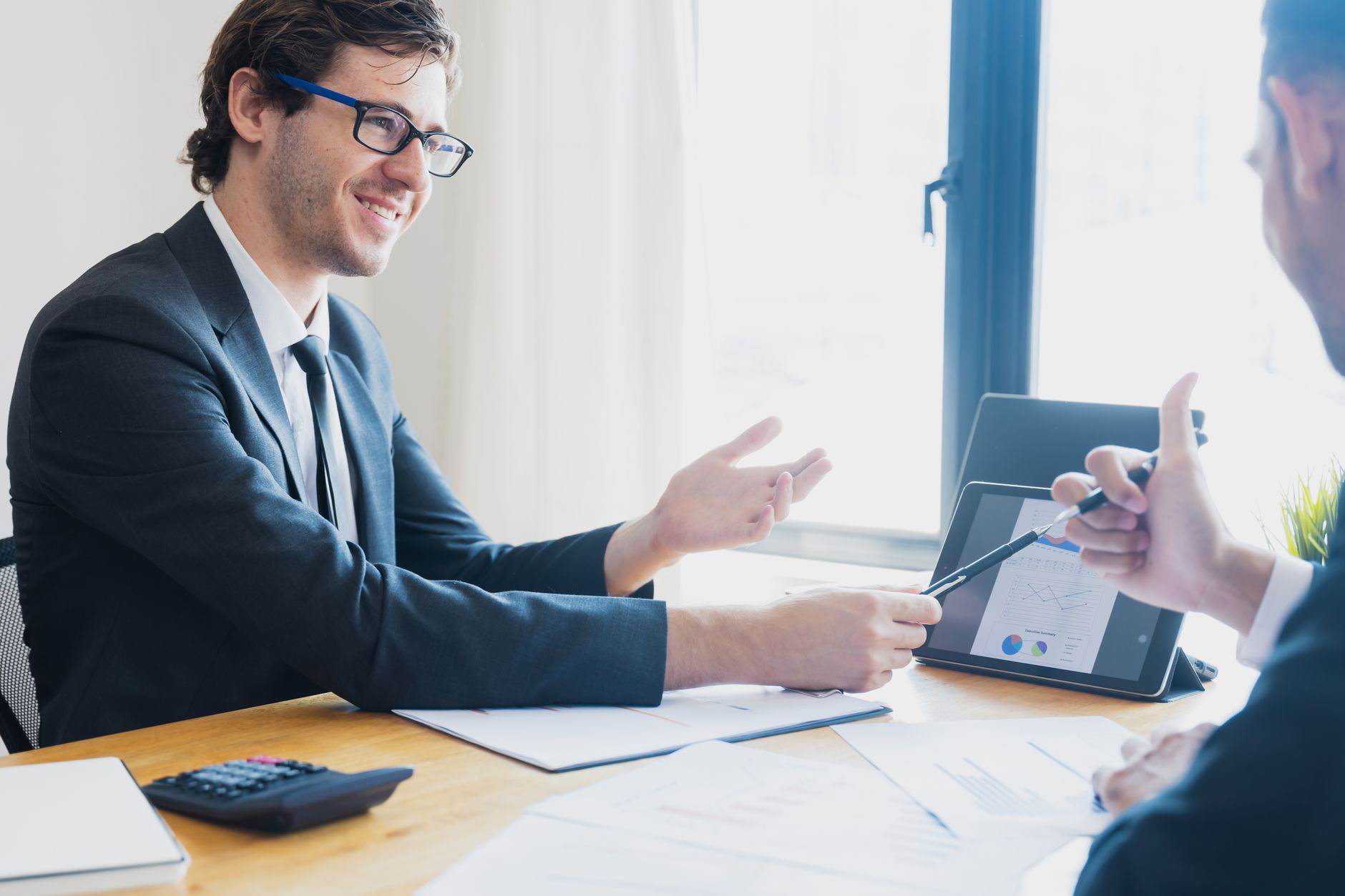 Two businessmen in formal attire discussing a business report in an office setting with a tablet. — Female Strength Unleashed