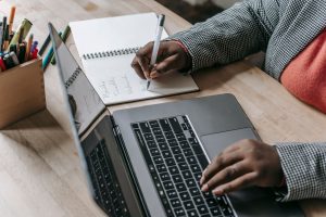 Crop unrecognizable African American female in formal wear writing notes in notepad while working on laptop — Finding the Bes