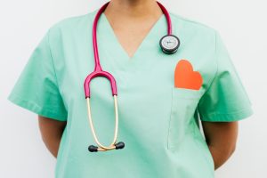 Close-up of a medical professional with a stethoscope and a paper heart cutout on a green uniform pocket. — Here are the thin