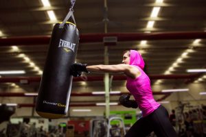 Athletic woman in pink activewear training with a punching bag at an indoor gym for fitness and exercise. — How to Get in Sha