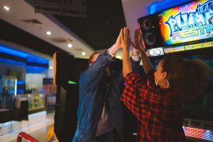 Energetic couple having fun at an arcade, sharing a high five and laughter. — Improve your chances of winning with PUBG Hacks