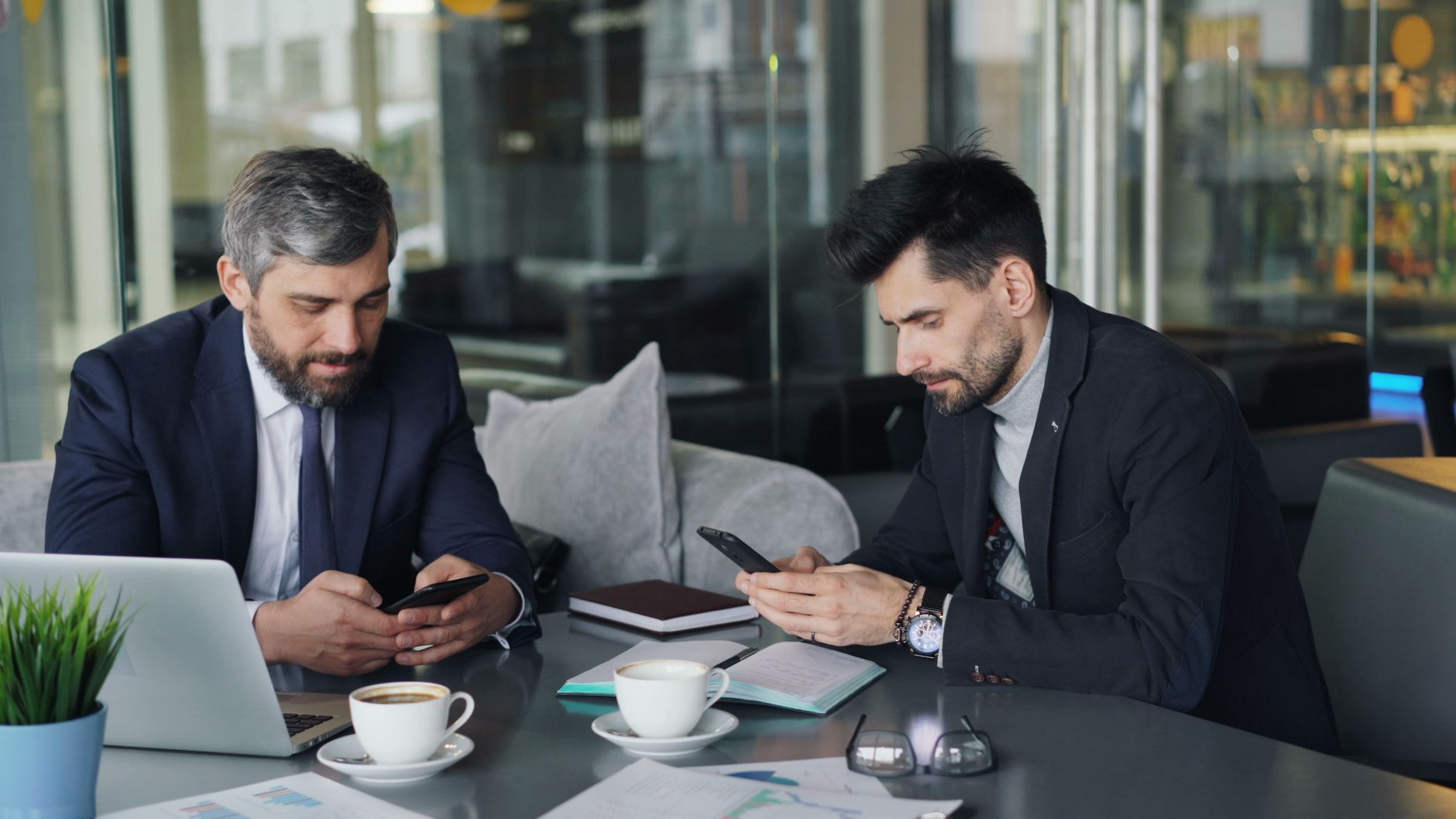 Two businessmen in a cafe working on smartphones and laptops, engaged in a meeting. — Instant Cash, Zero Hassle: Fastest E-Tr