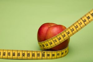 Red apple wrapped in a yellow measuring tape against a green backdrop emphasizes freshness and health. — Juice Diet - Detox a