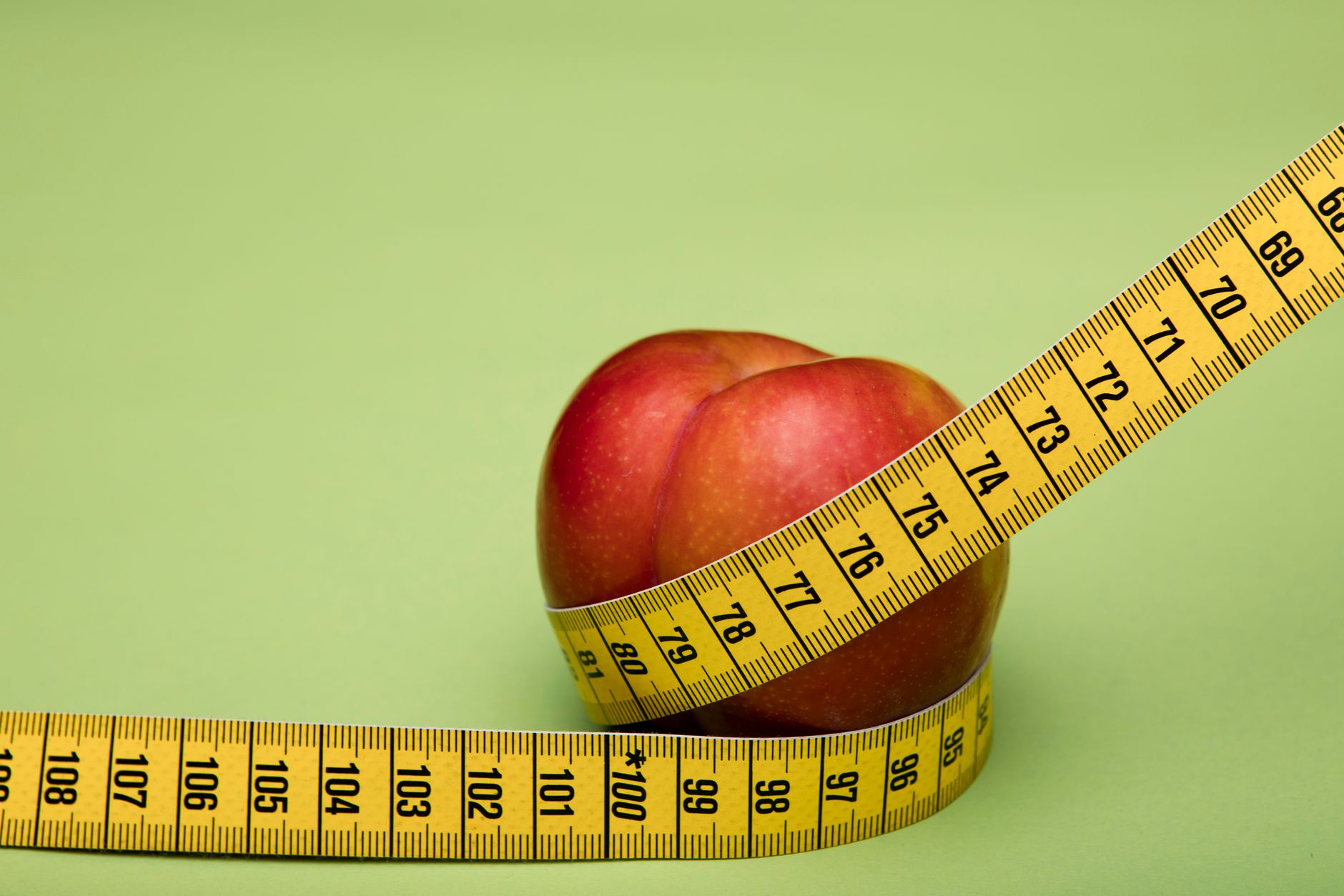 Red apple wrapped in a yellow measuring tape against a green backdrop emphasizes freshness and health. — Juice Diet - Detox a