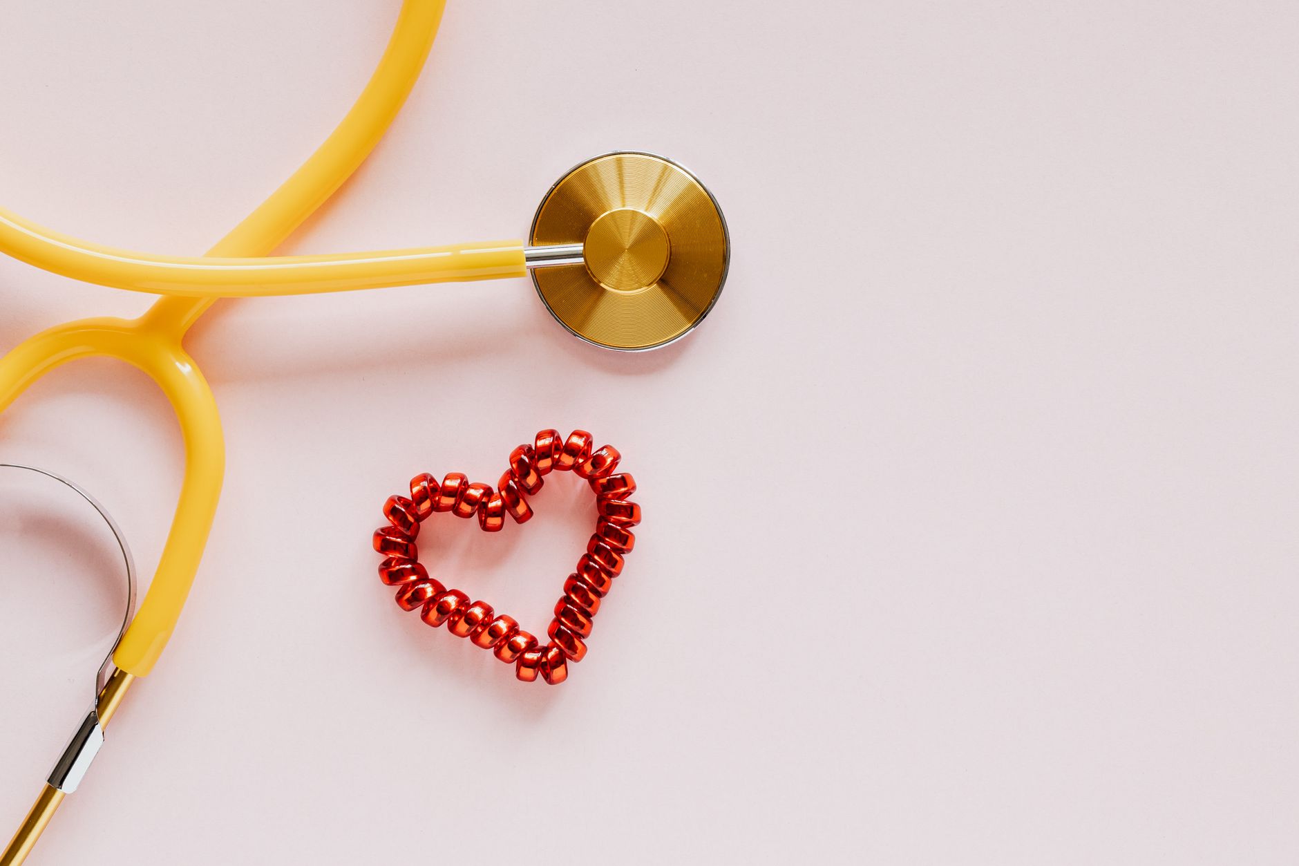 From above of yellow stethoscope near small red bead heart made for San Valentines Day on pale pink surface — Male pattern ba