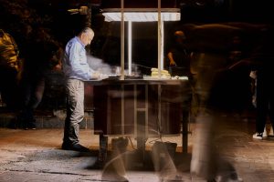 Street vendor cooking food at night with blurred people passing by. — Shaping Tomorrow's Healthcare: MSN in Nursing Practice