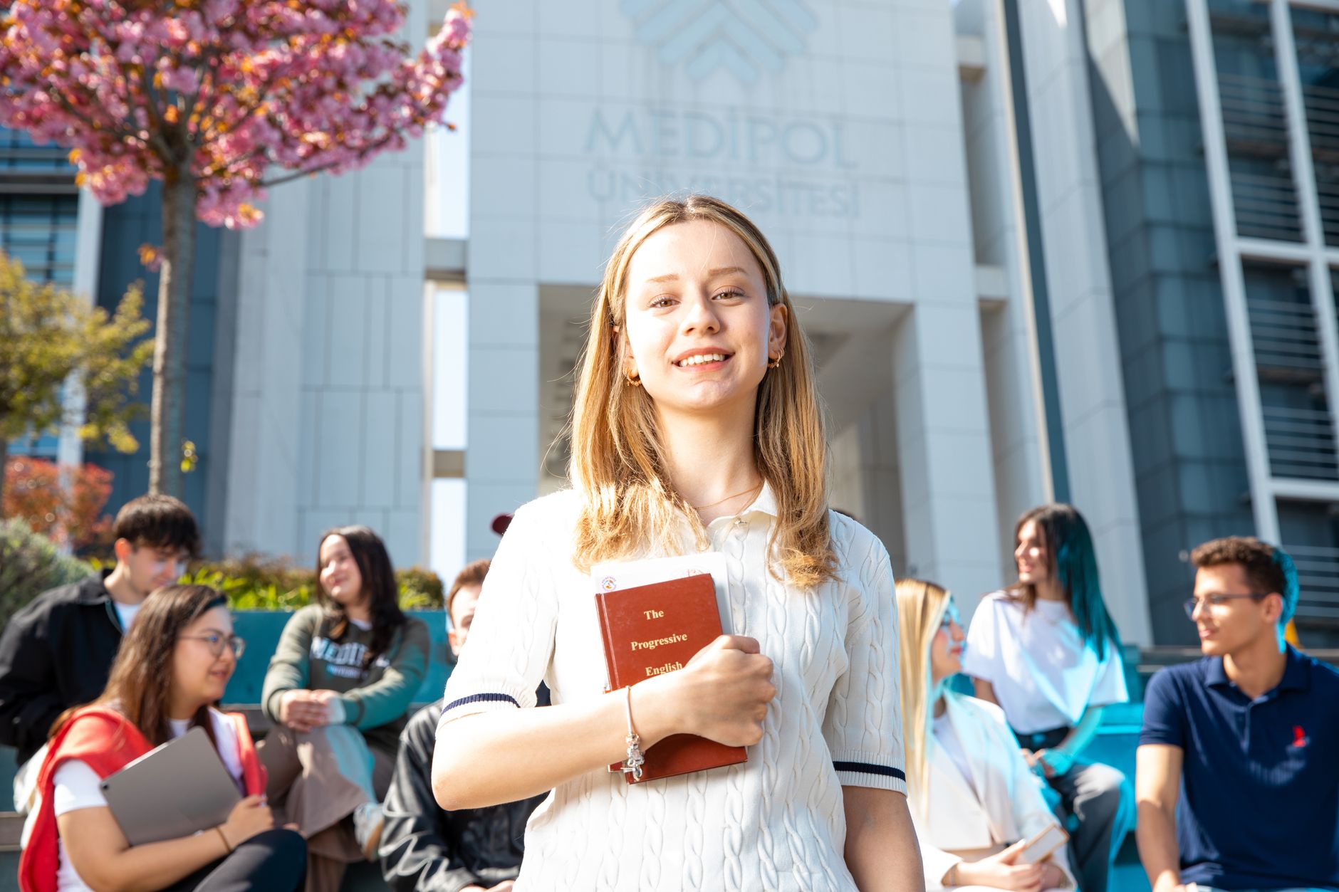 Happy university students socializing on campus, with a focus on a smiling young woman holding a book. — Decoding Med