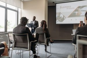 A business professional delivering a presentation in a conference room with diverse attendees. — UK Steroids Shops: E