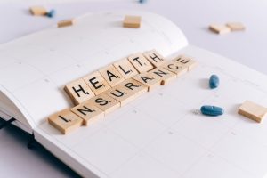Scrabble tiles spelling 'Health Insurance' on a calendar with pills. — Taking The First Step Toward Better Health: How Easy I