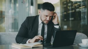 Focused businessman in suit multitasking on phone and laptop in modern office. — THC Syrup Blends Easily Into Drinks for Cust