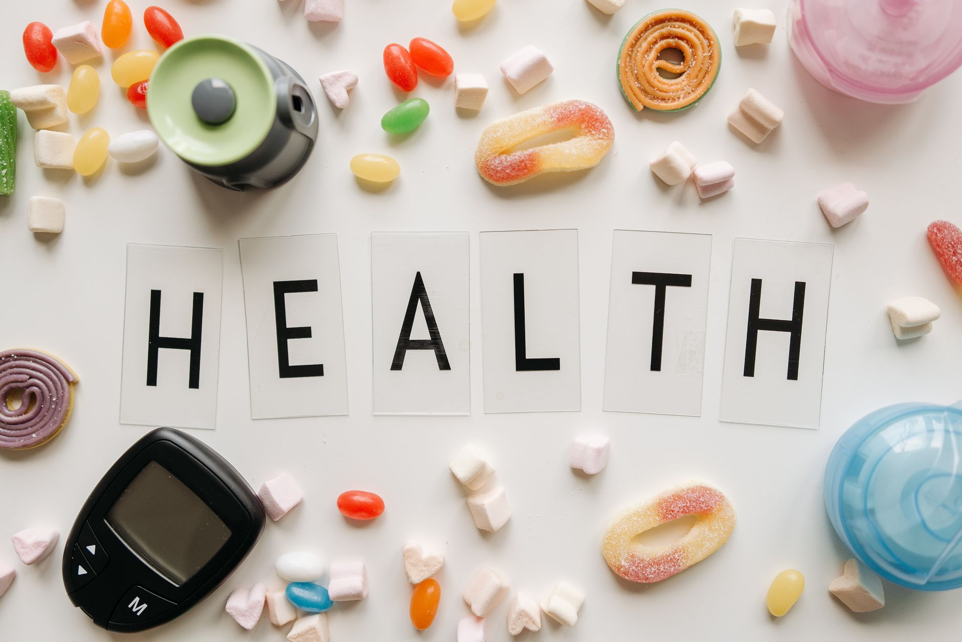 Creative flat lay with sweets around a 'HEALTH' text and monitoring device, symbolizing diabetes awareness. — The Importance