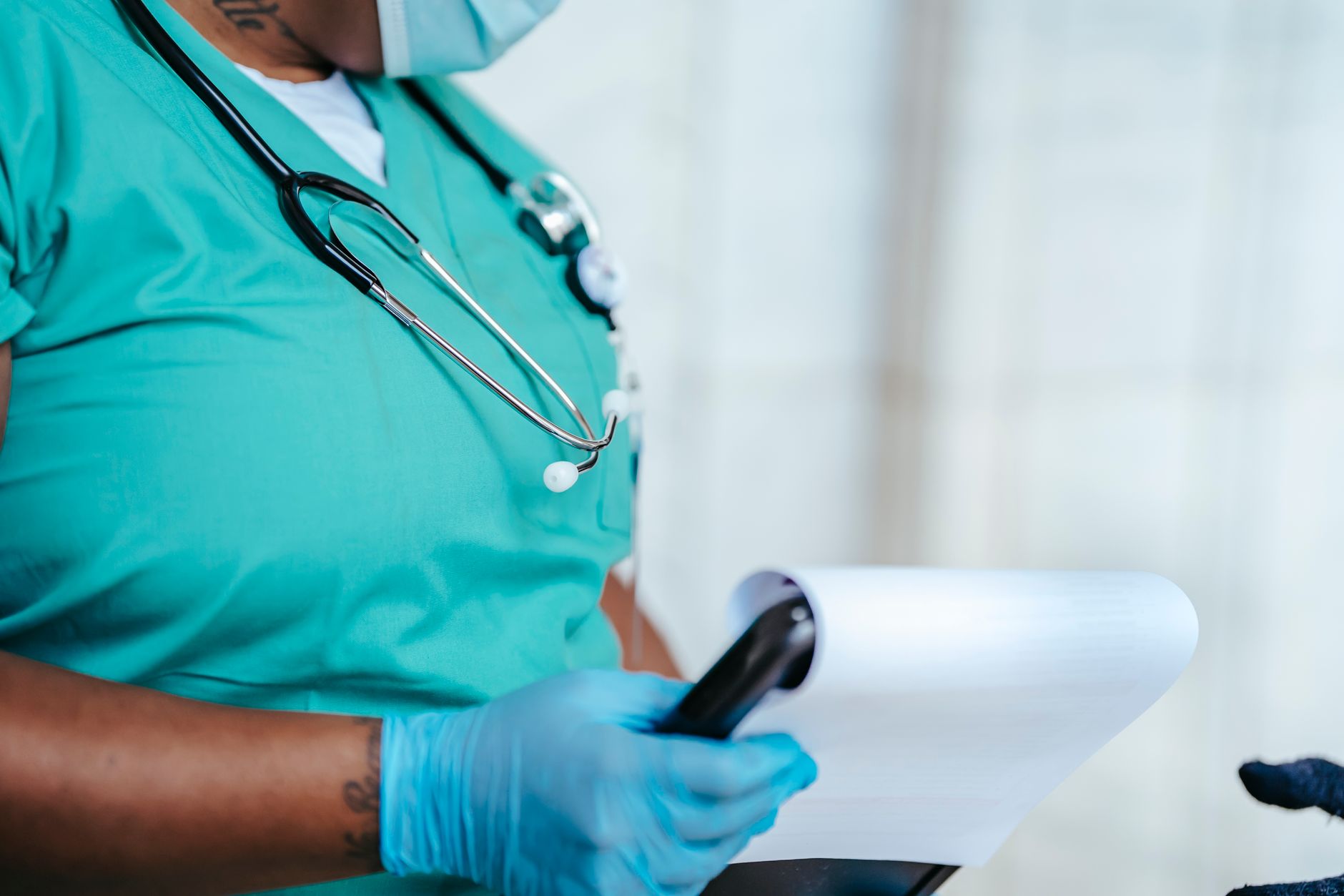 Side view of crop anonymous tattooed ethnic female medic in uniform with stethoscope and papers on clipboard — The Importance