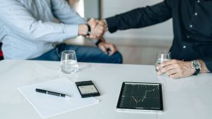 Business meeting with handshake and financial analysis displayed on a tablet. — The Psychosocial Benefits for Workers in Soch