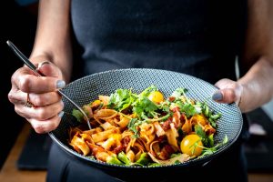 Close-up of woman holding a bowl of fresh pasta garnished with cilantro and cherry tomatoes. — The Raw Food Diet: A Comprehen