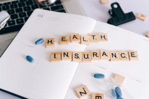 Scrabble tiles spelling 'Health Insurance' on planner with pills and laptop, symbolizing healthcare planning. — Tips to help