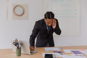 Professional businessman multitasking with phone and laptop at office desk, surrounded by documents. — Transforming Financial