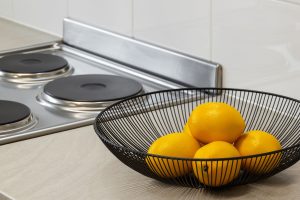 Lemons in a metal bowl on a kitchen counter beside an electric stove, highlighting freshness and simplicity. — Want to improv