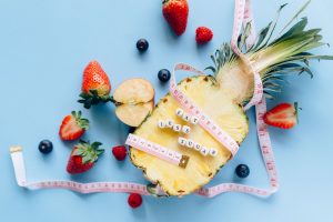 A sliced pineapple with berries and a tape measure on a blue background promoting healthy eating. — Which Diet Is Best For Yo