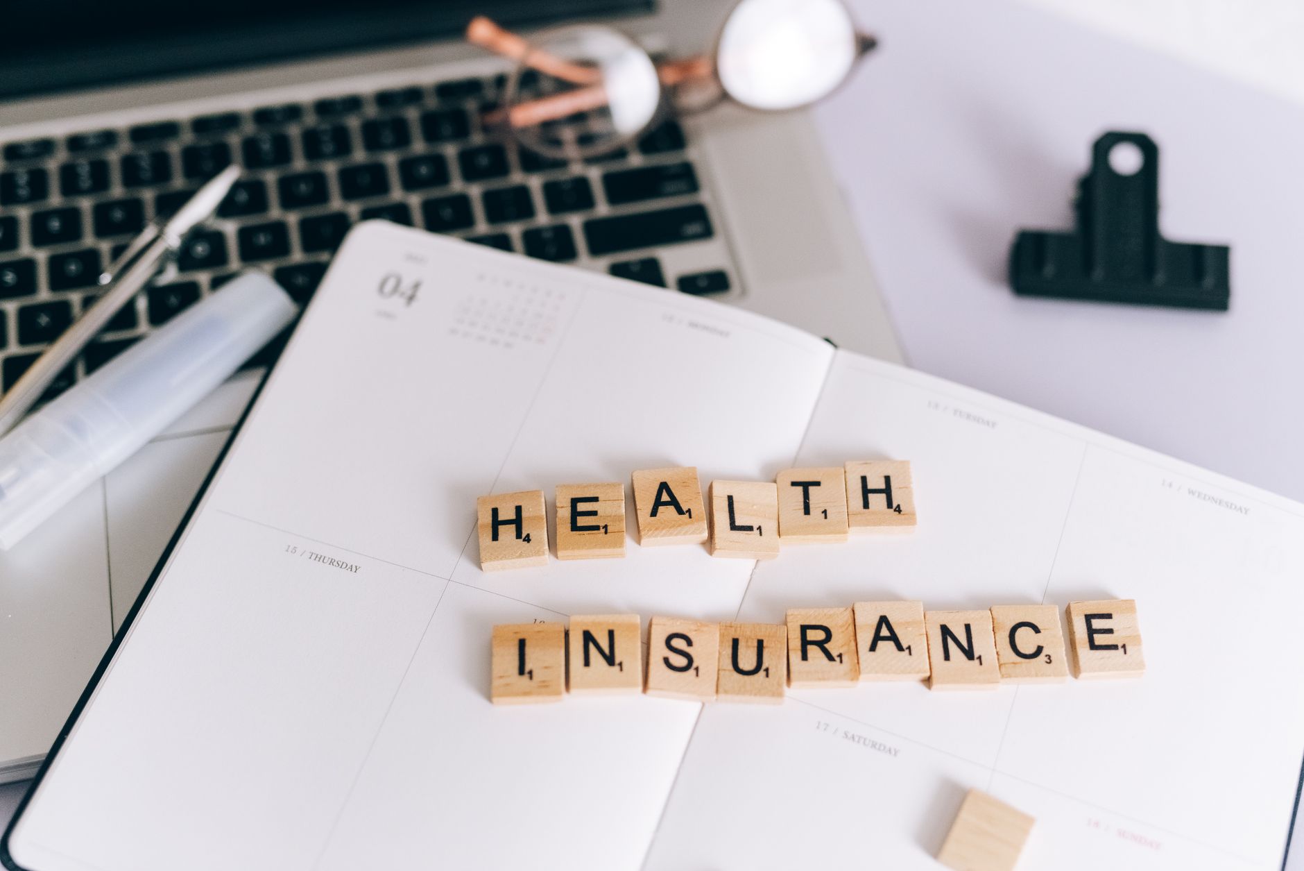 Close-up of Scrabble tiles spelling 'Health Insurance' on a planner with a laptop. — Why You Should Always Sterilize Your Too